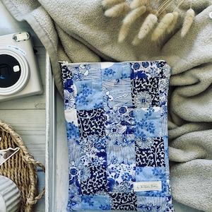 May include: A blue and white patchwork zippered pouch with floral patterns. The pouch is made of fabric squares in various shades of blue and white. The pouch is sitting in a white tray.