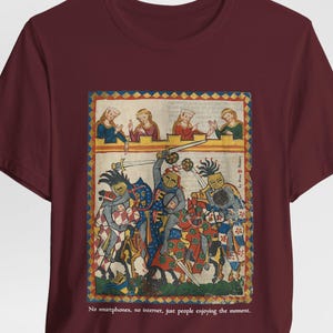 Puede incluir: Camiseta burdeos con una ilustración medieval de caballeros en batalla, con figuras observando desde arriba. El texto en la parte inferior dice: "Sin smartphones, sin internet, solo gente disfrutando el momento."
