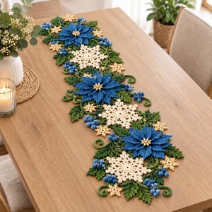 Puede incluir: Un camino de mesa largo y rectangular con un diseño de ganchillo que presenta flores de pascua azules, copos de nieve color crema, hojas verdes similares a helechos y racimos de pequeñas bayas azules en un patrón repetitivo.