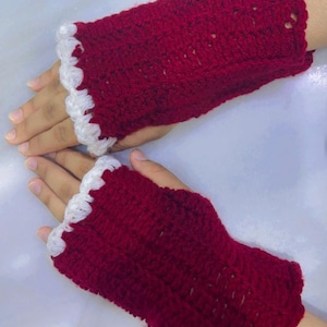 May include: A pair of fingerless gloves crocheted from deep red yarn, featuring a textured stitch pattern throughout the body and a decorative white scalloped edge trim along the opening where the fingers emerge from the garment.