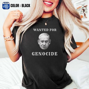 May include: Black t-shirt with the text "WANTED FOR GENOCIDE" above and below a grayscale portrait. The top left corner has a small logo that says "Daily Stitch US" and the words "COLOR: BLACK".