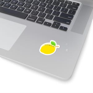 May include: A yellow lemon sticker with a white border, green leaf, and the text "lemonlyme.com" in a handwritten style. The sticker is placed on a silver laptop.