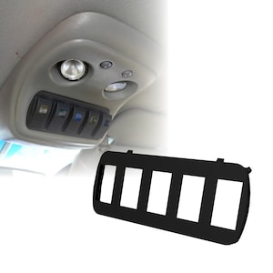Puede incluir: Panel de interruptores de plástico negro con cinco aberturas rectangulares. El panel está diseñado para encajar en el interior de un vehículo, como se ve en el fondo con los interruptores y luces existentes. El panel se muestra por separado para mayor claridad.