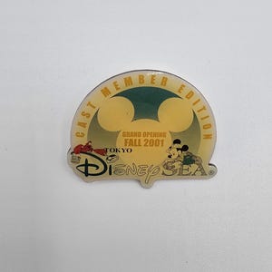 May include: A Disney Sea Cast Member Edition pin. The pin features Mickey Mouse and Donald Duck, with the text "Grand Opening Fall 2001 Tokyo". The pin has a yellow and green color scheme with the Disney Sea logo.