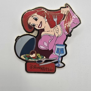 May include: A metal enamel pin featuring a cartoon character with long red hair wearing a pink dress, holding a silver fork to their hair. A silver platter with food, a blue goblet, and a knife are present. The text Disneyland Resort is printed below.