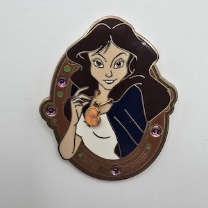 May include: Enamel pin featuring a cartoon woman with brown hair and a navy blue jacket. She wears a gold necklace with an orange heart pendant. The pin is framed in a brown oval with purple accents.