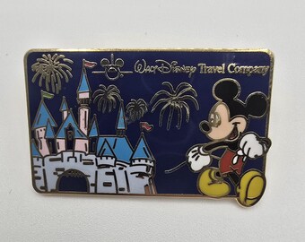 Vintage official Disney pin of Mickey Mouse next to the Magic Kingdom with fireworks above. It says "Walt Disney Travel Company."