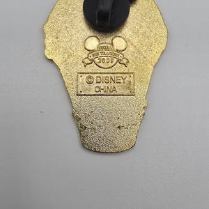 May include: A gold-toned metal pin back featuring a black Mickey Mouse-shaped rubber clutch. The back is embossed with the text Official Pin Trading 2008 and a rectangular box containing the text Disney China, indicating its origin and production year.
