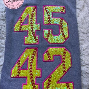May include: Gray sweatshirt with the numbers 45 and 42 in a softball design. The numbers are yellow with red stitching and outlined in pink. The sweatshirt has a circular logo in the upper left corner that says "Made with Love" and "The Coquette Embroidery".