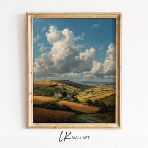 Puede incluir: Una pintura de paisaje enmarcada representa una escena rural con colinas, campos y un camino sinuoso. El cielo es azul vibrante con grandes nubes blancas y esponjosas. El marco es de color madera claro y cálido. El texto "LK WALL ART" está en la esquina inferior izquierda.