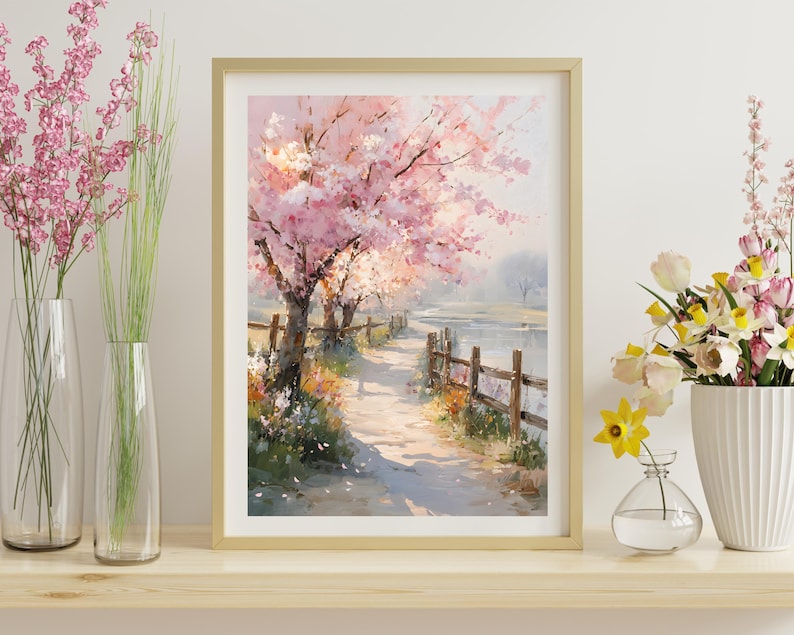 May include: A framed watercolor painting depicts a path along a river lined with blossoming pink cherry trees. A wooden fence borders the path. The painting is in a gold frame and is displayed on a wooden shelf with vases of flowers.