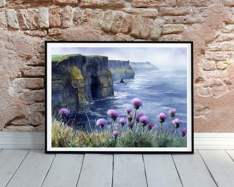May include: A framed watercolor print of the Cliffs of Moher in Ireland. The artwork depicts the dramatic cliffs meeting the ocean, with purple wildflowers in the foreground. The sky is a soft blue, and the water is a deep blue.