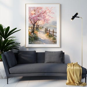 May include: A framed watercolor painting depicts a serene pathway lined with blossoming pink cherry trees. A wooden fence borders the path, leading to a body of water. The artwork is displayed above a dark gray sofa with pillows.