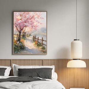 May include: A framed watercolor painting depicts a serene landscape with a path, wooden fence, and blossoming pink trees. The artwork is set against a soft, neutral background, creating a calming atmosphere. The painting is displayed above a bed.
