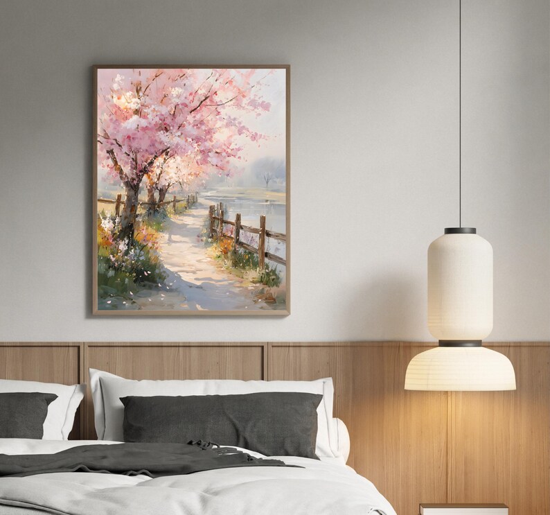 May include: A framed watercolor painting depicts a serene landscape with a path, wooden fence, and blossoming pink trees. The artwork is set against a soft, neutral background, creating a calming atmosphere. The painting is displayed above a bed.