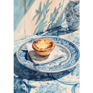 Puede incluir: Pintura a la acuarela de una tarta de crema portuguesa sobre una servilleta blanca, colocada sobre un plato con estampado azul y blanco. El plato está sobre una mesa con un diseño floral a juego. Un jarrón azul y blanco está en el fondo.