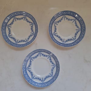 May include: Three white porcelain saucers with a blue floral design around the rim and center. The blue pattern includes small flowers and decorative borders. These saucers are likely part of a vintage tea set.