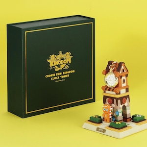 Puede incluir: Una figura decorativa de torre del reloj con un hombre de jengibre y un reloj de bolsillo. La torre del reloj es marrón, naranja y blanca, con una base verde. La caja es de color verde oscuro con letras doradas que dicen "Cookie Run: Kingdom Clock Tower."