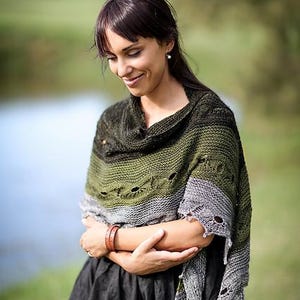 Puede incluir: Una mujer con un chal verde, gris y negro con un diseño de punto texturizado. El chal tiene un efecto degradado, que va del verde oscuro al gris. La mujer lleva un vestido negro y una pulsera de cuero marrón.