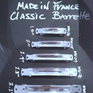Peut inclure: Plusieurs barrettes classiques argentées, fabriquées en France, de différentes tailles, de 40 mm à 90 mm. Le texte "The Barrette Factory" et "CLASSIC BARRETTE" est visible.