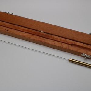May include: A wooden box with a brass rod inside. The box is open and the rod is lying on a white surface.