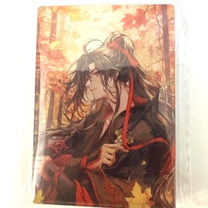 May include: A rectangular card featuring an illustration of two figures in traditional attire, set against a backdrop of a forest with autumn foliage. The figures have long black hair and are wearing red and black clothing.