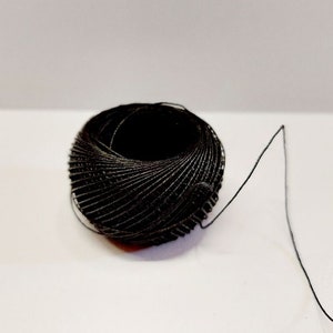 Op de afbeelding: Een zwarte spoel garen met een lange draad die eruit steekt.