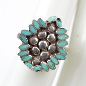 May include: A silver ring featuring a cluster of seven smooth, rounded silver spheres at the center, surrounded by a border of small, oval-shaped turquoise stones arranged in a petal-like pattern around the metallic centerpiece.