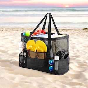 May include: Black mesh beach tote bag with multiple pockets, filled with yellow flip-flops, sunglasses, and other beach essentials. The bag has sturdy black handles and is set on a sandy beach with the ocean in the background.