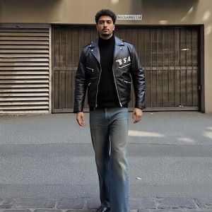 May include: A black leather jacket with the text "BSA" on the chest, paired with a black turtleneck sweater and blue jeans. The person is wearing black shoes. The outfit is a classic, edgy style.