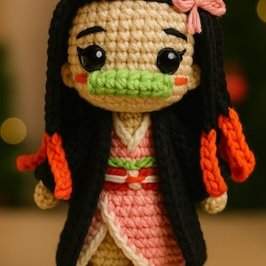 Puede incluir: Muñeca de ganchillo que representa un personaje con piel bronceada, cabello negro y un lazo rosa. La muñeca viste un kimono rosa y blanco, con protector bucal verde y detalles en naranja. La muñeca mide unos 15 cm de alto.