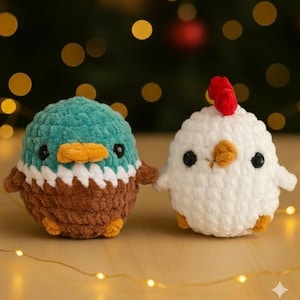 May include: Two handmade crochet stuffed animals: a teal and brown duck and a white chicken. The duck has a teal head, brown body, and orange beak. The chicken has a red comb and orange beak. Both have black eyes and are holding hands.