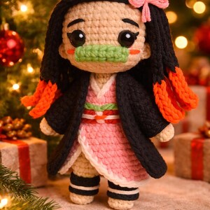 May include: A handmade crochet doll with black hair, orange accents, and a pink bow. The doll wears a pink and white kimono with a black overcoat and green mouth cover. The doll is standing in front of a Christmas tree.