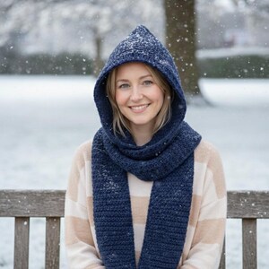 Könnte beinhalten: Ein marineblauer Kapuzenschal und ein passender Schal werden über einem beige-weiß gestreiften Pullover getragen. Die Frau lächelt in einer verschneiten Umgebung im Freien. Der Schal und die Kapuze scheinen aus dickem Strickmaterial zu sein.