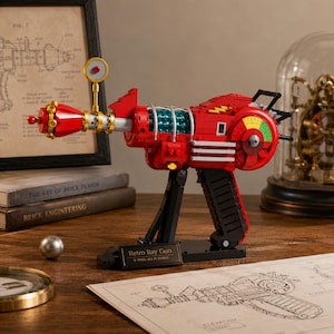 May include: A red and black toy ray gun constructed from building bricks, featuring a teal translucent cylinder, a yellow lightning bolt emblem, and a circular gauge with green, yellow, and red segments. A black plaque reads Retro Ray Gun.