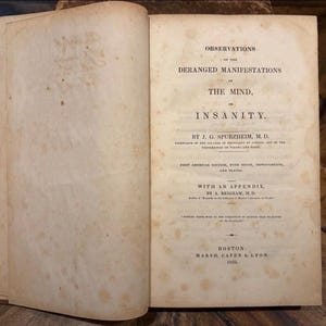 May include: An open antique book with aged, off-white pages featuring brown foxing spots. The title page reads: Observations on the Deranged Manifestations of the Mind, or Insanity, by J. G. Spurzheim, M.D., published in Boston by Marsh, Capen & Lyon, 1833.