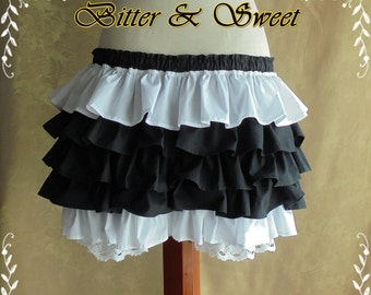 May include: A black and white layered ruffle skirt with a white lace trim. The skirt is on a wooden mannequin and has the text "Bitter & Sweet" above it.
