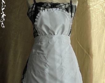 May include: A white apron with a lace trim and two pockets, worn over a black and white plaid dress with a black lace trim. The dress has a scoop neckline and thin straps.