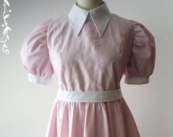 May include: A pink dress with a white collar and white trim around the sleeves and waist. The dress has a full skirt and is made of a lightweight fabric.
