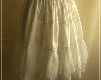 May include: White layered tulle skirt with a satin ribbon trim. The skirt is on a white mannequin and has a ruffled hem.