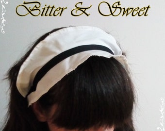 May include: A white fabric headband with a black band around the top. The headband is worn on a person's head with their black hair covering most of the headband.
