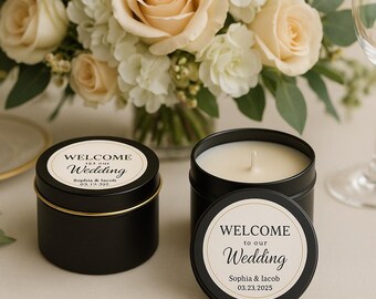 May include: Two black metal candle tins with cream-colored wax. Each lid features a circular label with the text "WELCOME to our Wedding", "Sophia & Iacob", and the date "03.23.2025" printed in black ink against a light beige background.