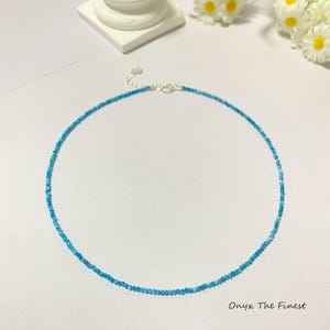 May include: A delicate necklace featuring small, round, light blue beads. The necklace has a silver clasp and is displayed on a white surface. The text "Onyx The Finest" is in the bottom right corner. This piece is a fine jewelry item.