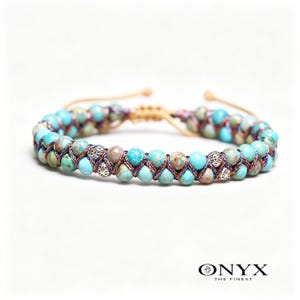 May include: A double-strand bracelet featuring turquoise and brown beads, woven together with a beige cord. The bracelet has silver-colored accents and is set against a white background. The brand name "ONYX THE FINEST" is at the bottom.
