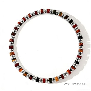 May include: A circular bracelet with a silver band and a mosaic of rectangular, colorful stones. The stones are in shades of red, orange, black, and green. The text "Onyx The Finest" is in the bottom right corner.
