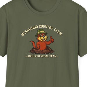 May include: Olive green t-shirt featuring a cartoon gopher wearing a hat and giving a thumbs-up. The shirt displays the text "Bushwood Country Club" above the gopher and "Gopher Removal Team" below.