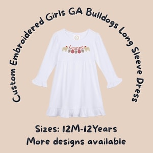 May include: White long-sleeved dress with frilled sleeves and hem. The dress has embroidered details including the name "Leanne", footballs, and bulldog graphics. Text on the image reads "Custom Embroidered Girls GA Bulldogs Long Sleeve Dress". Sizes available: 12M-12 Years.