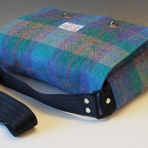 May include: A blue, green and purple plaid messenger bag with a black adjustable strap and silver hardware. The bag has a label that says "Woolrich".