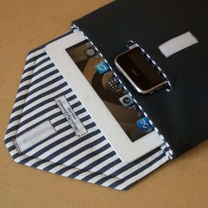 Peut inclure: Une pochette en tissu rayée noir et blanc avec une tablette blanche et un téléphone noir à l'intérieur. La pochette est dotée d'une fermeture velcro et d'une petite étiquette indiquant "Cuir véritable".