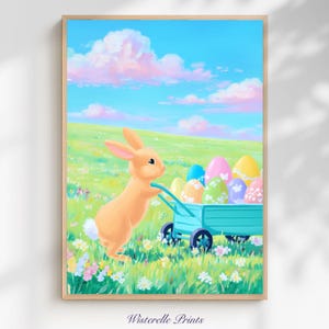 Puede incluir: Una impresión enmarcada que presenta un conejo de dibujos animados empujando un carro turquesa lleno de huevos de Pascua decorados a través de un campo de hierba. El cielo es azul con nubes. La impresión está firmada "Wisterelle Prints".
